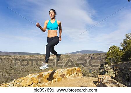 Stock Photography - Hispanic woman jumping in mid-air in remote area. Fotosearch