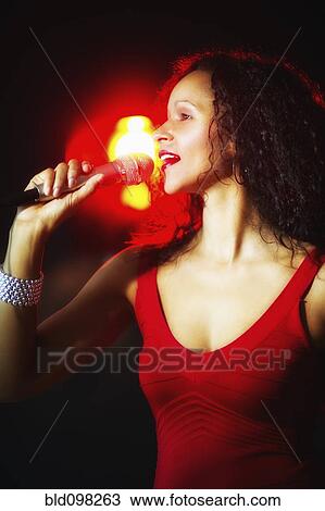 Stock Image - Hispanic woman singing in nightclub. Fotosearch
