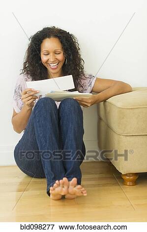 Stock Photo - Hispanic woman sitting on floor looking at mail. Fotosearch