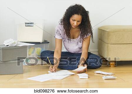 Stock Photograph - Hispanic woman sitting on floor paying bills. Fotosearch