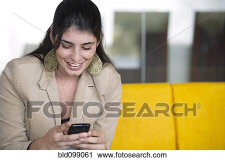 Stock Image - Hispanic woman text messaging on cell phone. Fotosearch