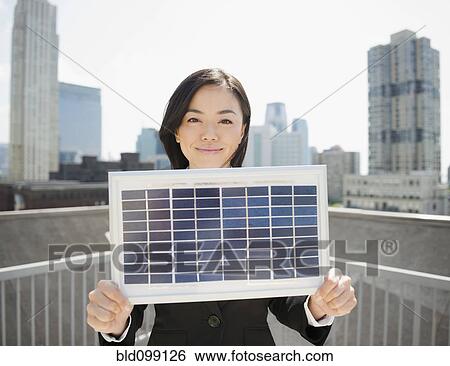 Stock Photograph - Japanese businesswoman holding solar panel outdoors. Fotosearch