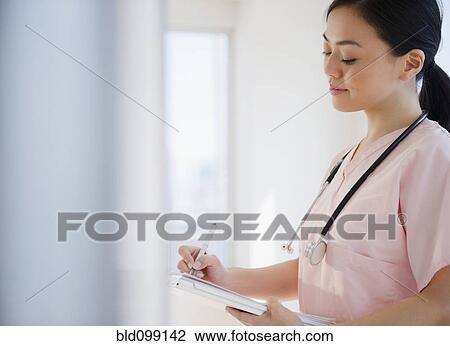 Stock Image - Japanese nurse writing on medical record. Fotosearch