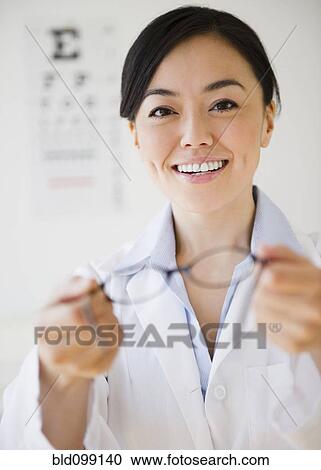 Stock Image - Japanese optometrist holding eyeglasses. Fotosearch