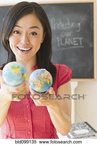 Stock Photography - Japanese teacher holding small globes in classroom. Fotosearch