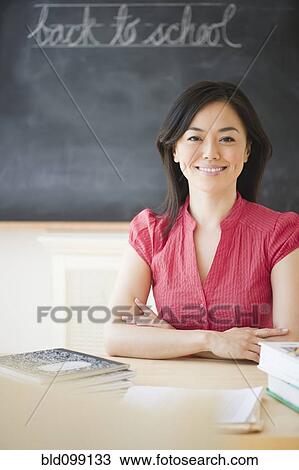 Stock Image - Japanese teacher sitting at desk in classroom. Fotosearch