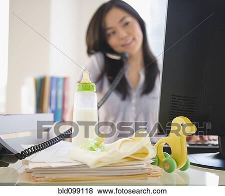 Stock Photo - Japanese woman on phone with baby toys on desk. Fotosearch