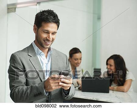 Stock Image - Mixed race businessman using cell phone in office. Fotosearch