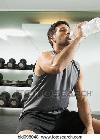 Stock Photo - Mixed race man drinking water in gym. Fotosearch