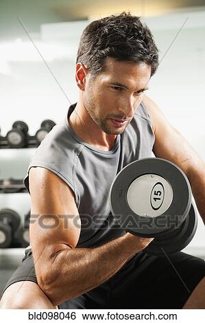 Stock Photograph - Mixed race man lifting dumbbells in gym. Fotosearch
