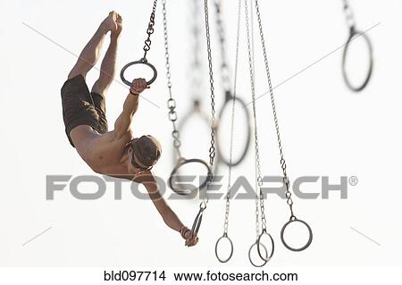 Picture - Mixed race man swinging on athletic rings. Fotosearch