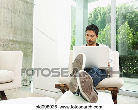 Stock Photograph - Mixed race man using laptop in living room. Fotosearch