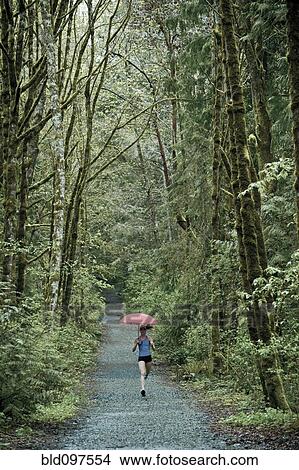 Picture - Mixed race runner training on remote road with umbrella. Fotosearch