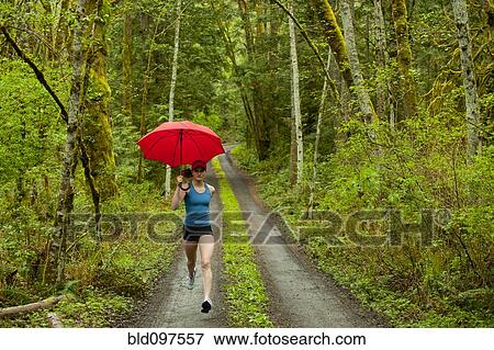 Stock Photo - Mixed race runner training on remote road with umbrella. Fotosearch