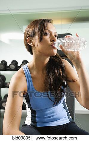 Stock Image - Mixed race woman drinking water in gym. Fotosearch