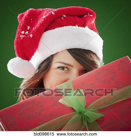 Stock Photography - Mixed race woman in Santa hat holding Christmas gift. Fotosearch