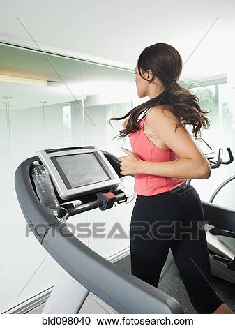 Stock Image - Mixed race woman running on treadmill. Fotosearch