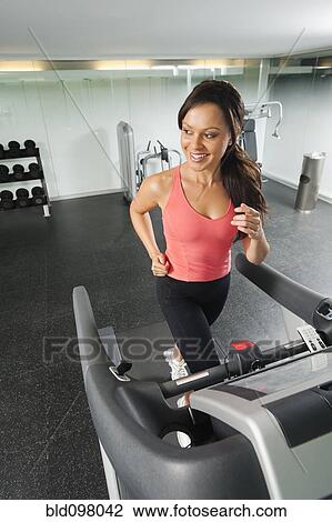 Stock Image - Mixed race woman running on treadmill. Fotosearch