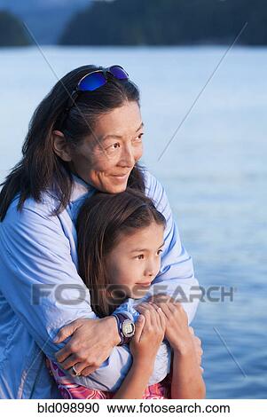 Stock Image - Mother and daughter hugging near lake. Fotosearch