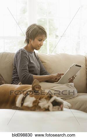 Stock Image - Native American woman using digital tablet on sofa. Fotosearch