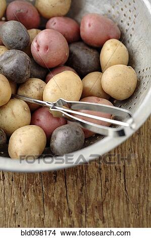 Picture - Peeler in colander with multicolored potatoes. Fotosearch
