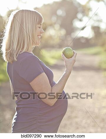 Pregnant Caucasian woman eating apple outdoors View Large Photo Image Stock Image - Pregnant Caucasian woman eating apple outdoors. Fotosearch