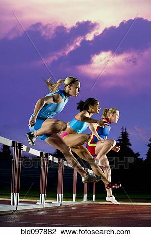 Stock Image - Runners jumping hurdles in race. Fotosearch