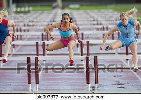 Stock Photo - Runners jumping hurdles in race. Fotosearch