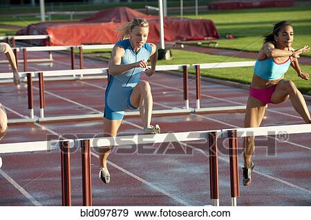 Stock Photo - Runners jumping hurdles in race. Fotosearch