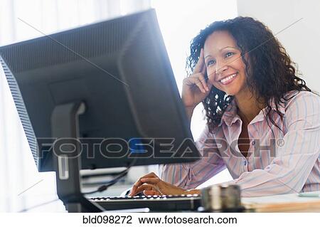 Stock Image - Smiling Hispanic businesswoman using computer at desk. Fotosearch