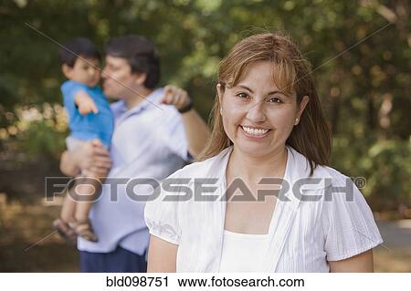 Stock Image - Smiling Hispanic woman outdoors with family. Fotosearch