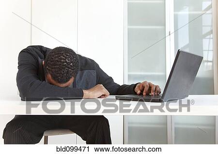 Stock Image - Tired Black businessman sleeping near laptop. Fotosearch