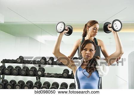 Stock Image - Trainer helping woman to use dumbbells. Fotosearch