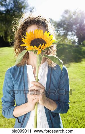 Stock Image - Woman holding sunflower in front of her face. Fotosearch