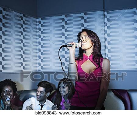 Stock Image - Woman singing karaoke in nightclub. Fotosearch