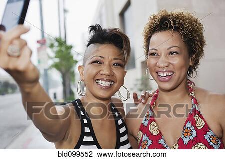 Stock Image - Women taking self-portrait with camera phone. Fotosearch
