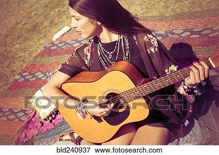 Stock Photo - Asian woman sitting on blanket playing guitar. Fotosearch