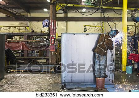 Stock Image - Asian worker grinding metal container in factory. Fotosearch