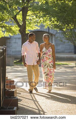 Stock Image - Black couple holding hands walking in park. Fotosearch