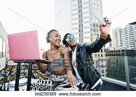 Black DJ and man posing for cell phone selfie on urban rooftop View Large Photo Image Stock Photo - Black DJ and man posing for cell phone selfie on urban rooftop. Fotosearch