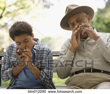Stock Image - Black grandson and grandfather playing harmonica together in park. Fotosearch