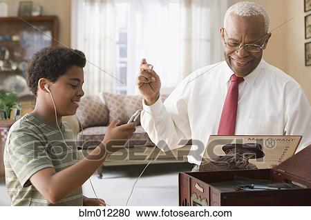Stock Image - Black grandson and grandfather listening to record player. Fotosearch