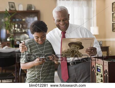 Stock Image - Black grandson and grandfather listening to record player. Fotosearch