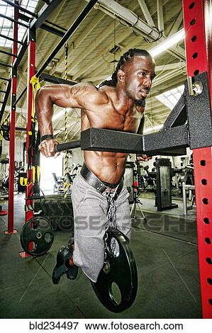 Stock Photo - Black man doing weighted push-up in gymnasium. Fotosearch
