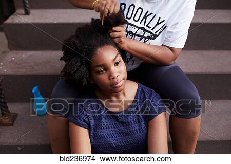 Picture - Black mother styling hair of daughter on staircase. Fotosearch
