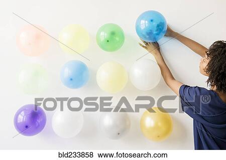 Stock Photo - Black woman attaching balloons to wall. Fotosearch