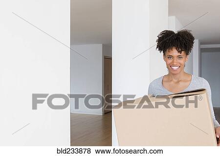 Stock Photo - Black woman carrying cardboard box in empty apartment. Fotosearch