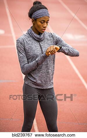Stock Photo - Black woman checking smart watch on track. Fotosearch