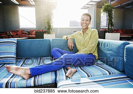 Stock Photography - Black woman laughing on rooftop sofa. Fotosearch