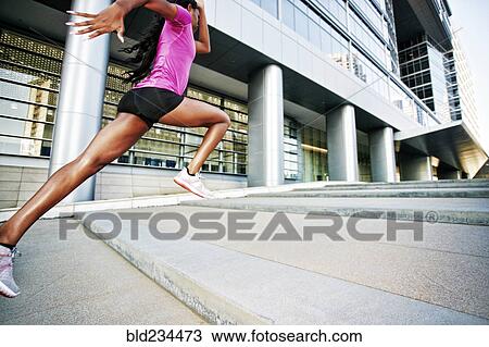 Stock Image - Black woman running and jumping on city staircase. Fotosearch
